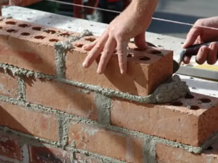 Hands setting a red brick into fresh mortar
