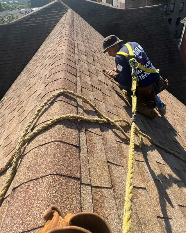 Roofer in a safety harness laying ridge shingles
