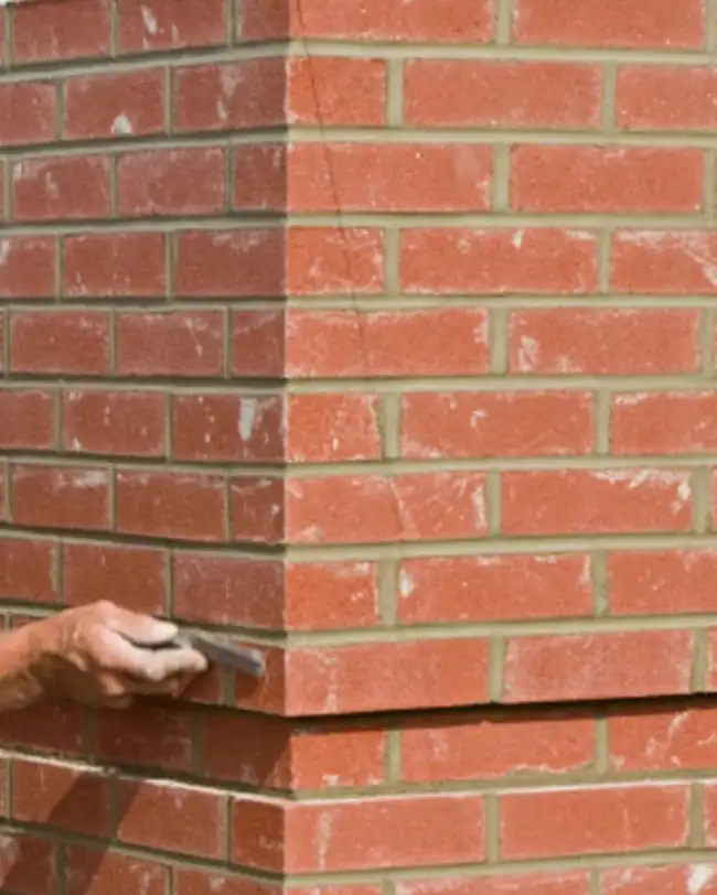 A mason pointing the mortar joints of a red brick pier